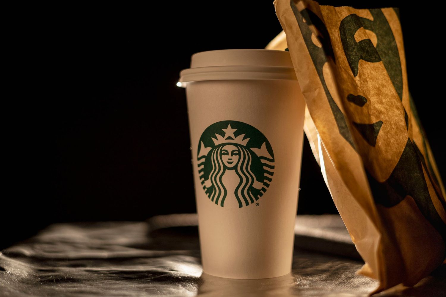 Starbucks coffee cups and pastries arranged on a dark surface with dramatic lighting.