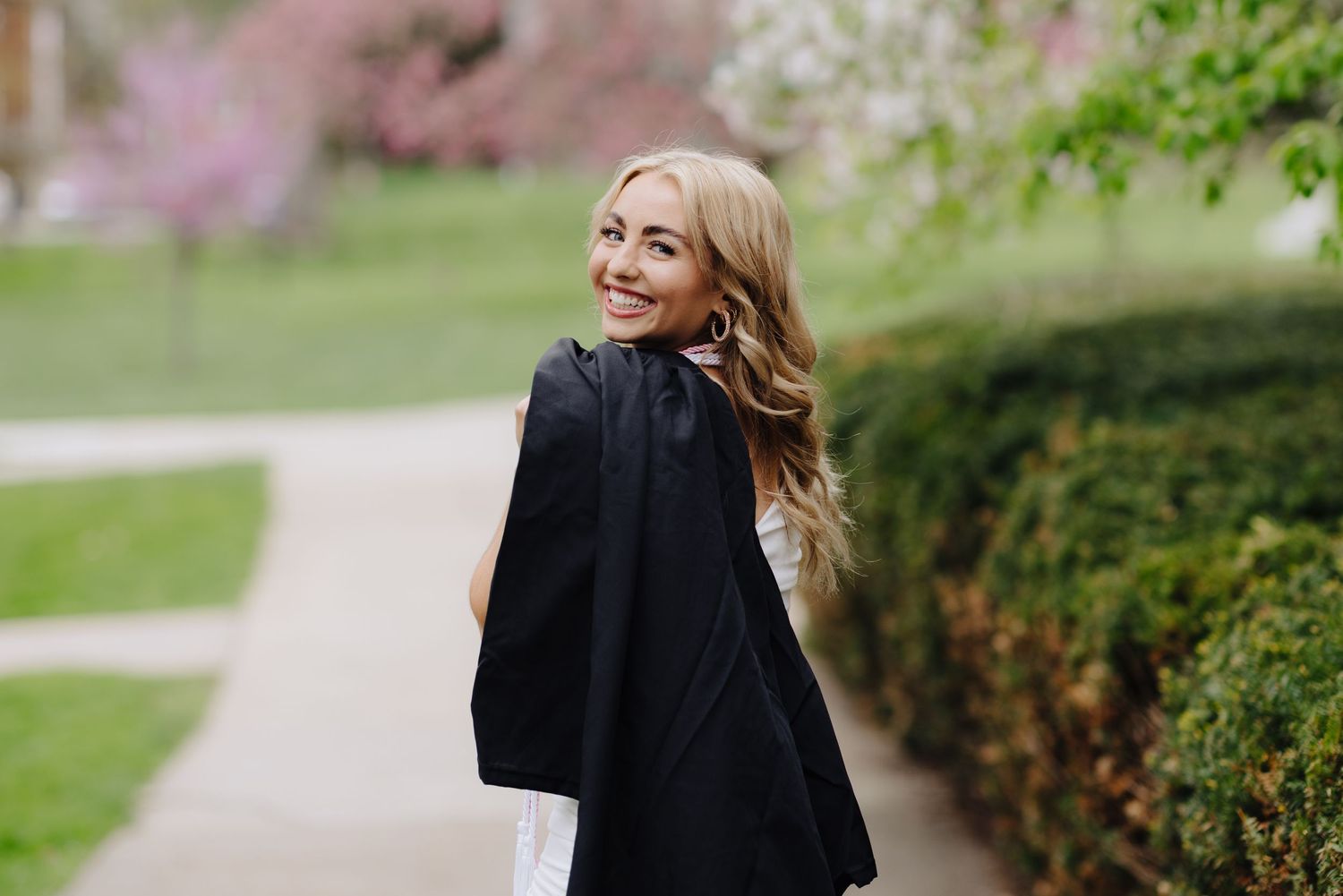 Woman in black jacket smiling over shoulder while walking through spring gardens.