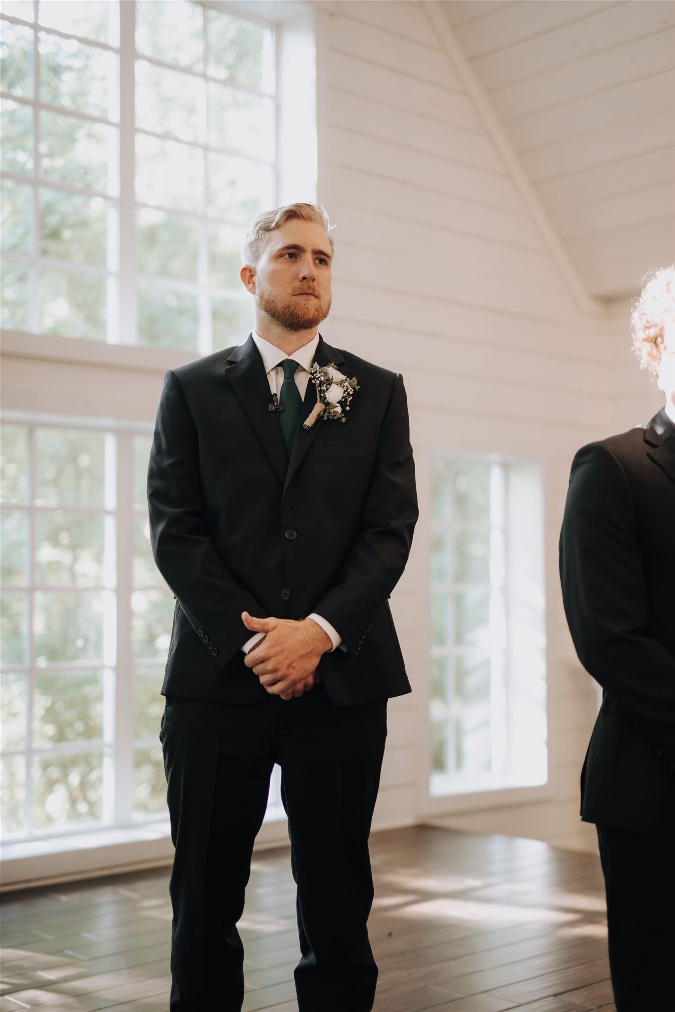 A groom stands solemnly at the altar wearing a black suit with boutonniere.