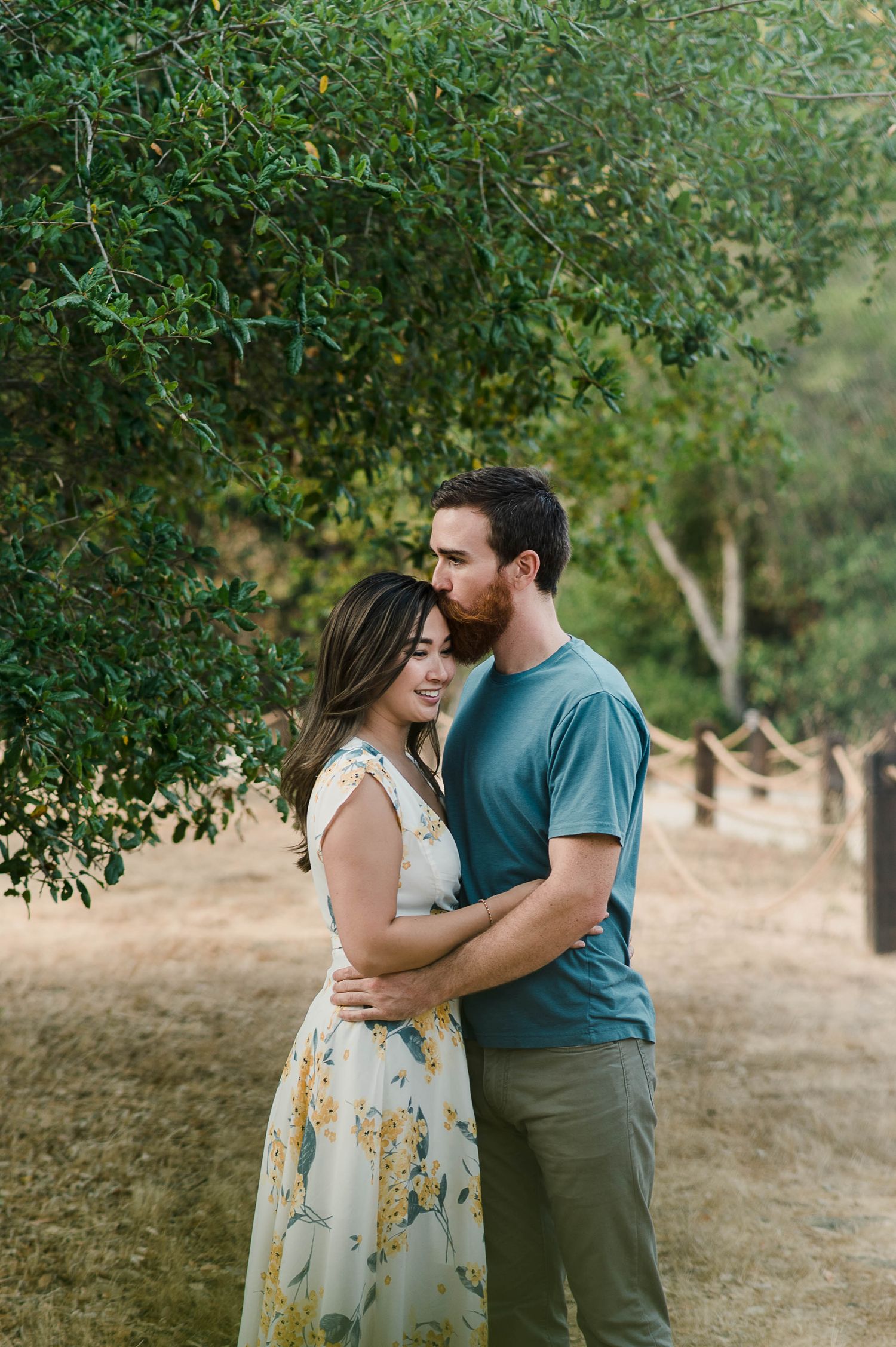 A romantic embrace under green trees on a sunlit summer afternoon.