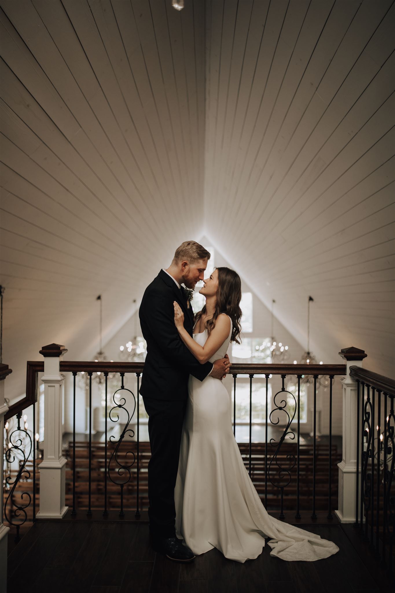 Romantic wedding portrait in front of vaulted ceiling with dramatic lighting and iron railing details.