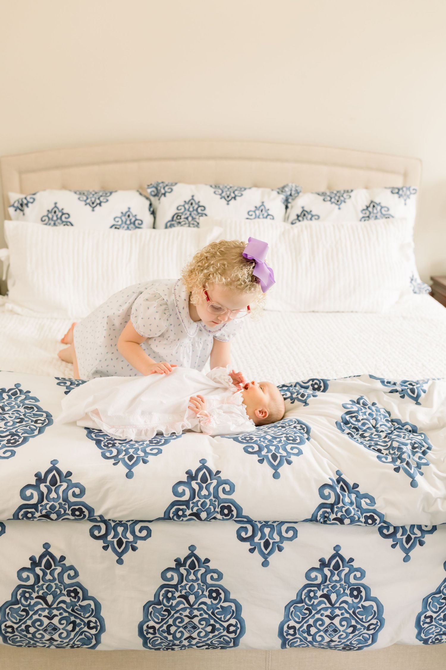 Two children playing together on a white bed with blue damask print bedding.