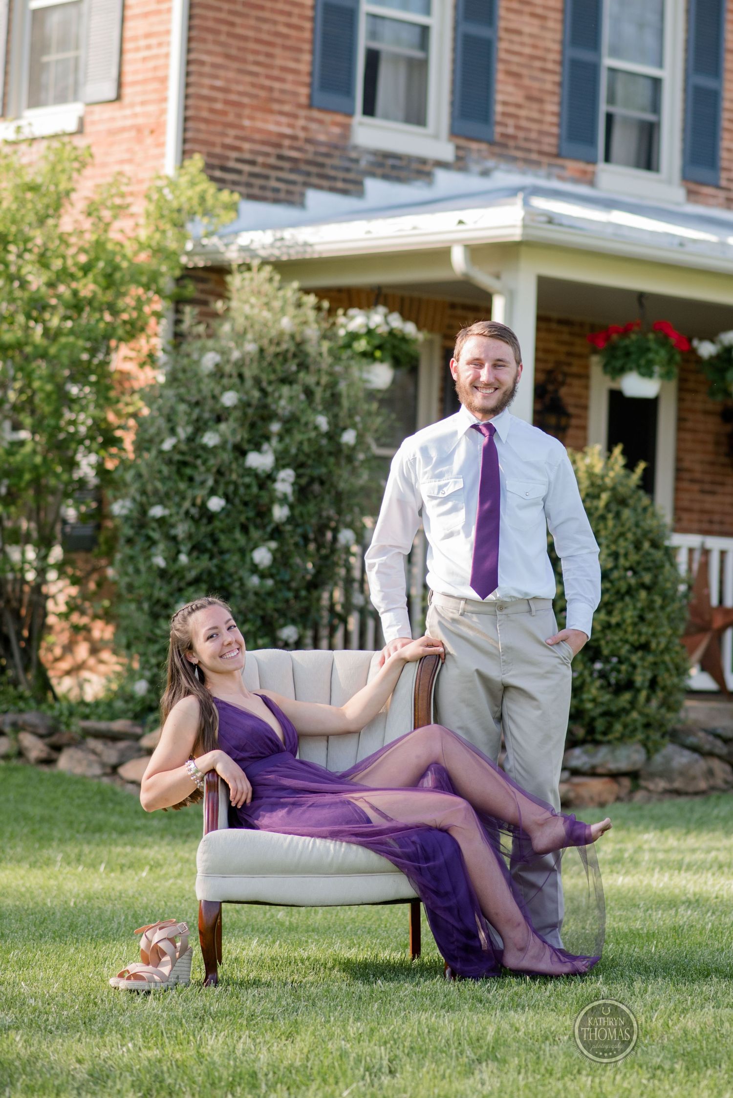 Elegant outdoor portrait with woman seated in purple gown and man standing in formal attire.