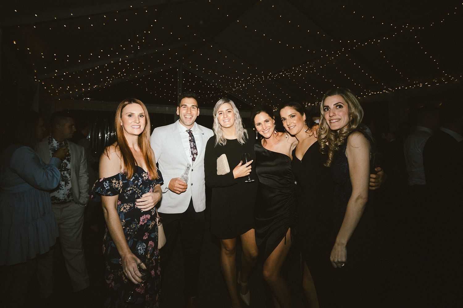 Party guests celebrate on the dance floor under twinkling lights at an evening event.