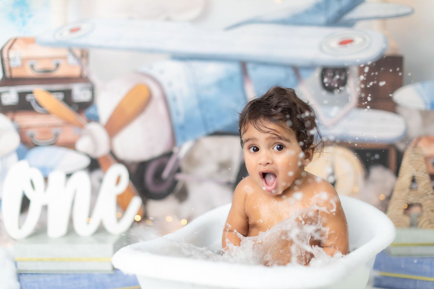 Candid moment of baby splashing in a milk bath surrounded by white decorations.