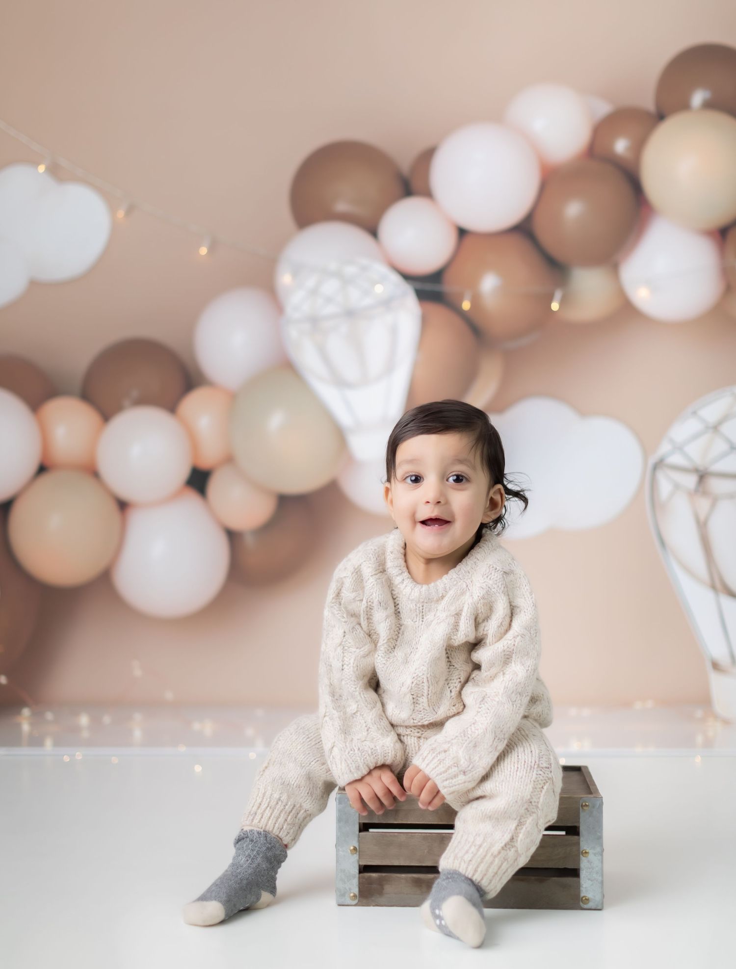 Rustic wooden crate with balloon arch and hot air balloon decorations in neutral tones.