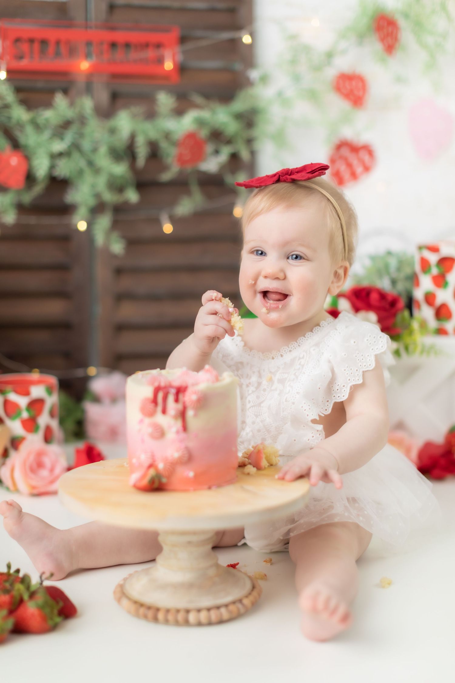 Pink and white cake smash photography setup with strawberries and floral decorations.