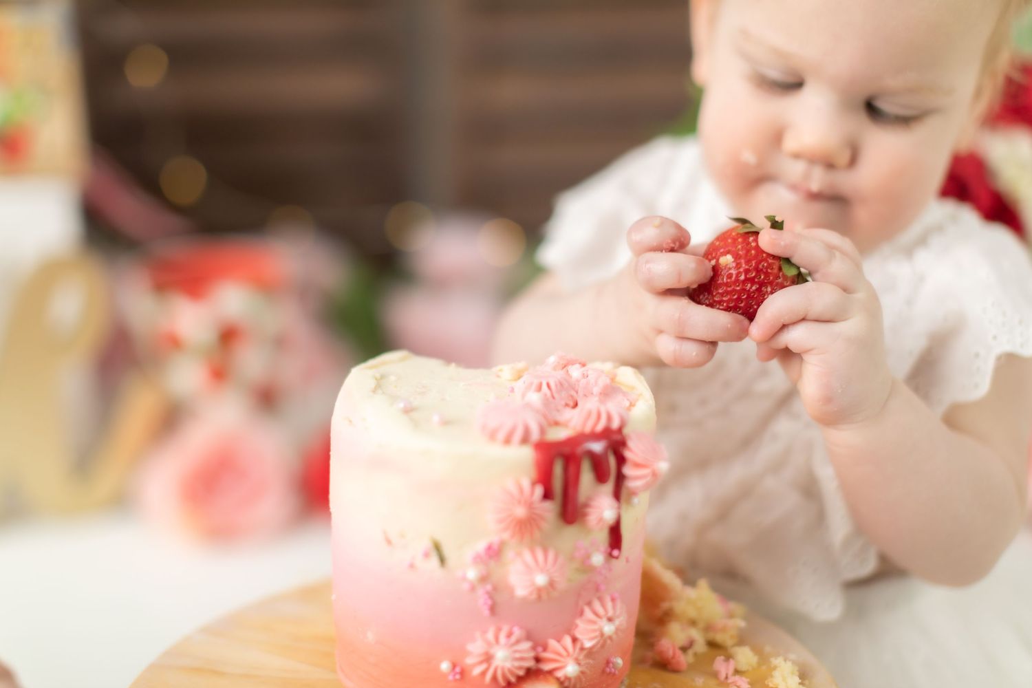 Close-up of pink cake being smashed with tiny hands and strawberries.