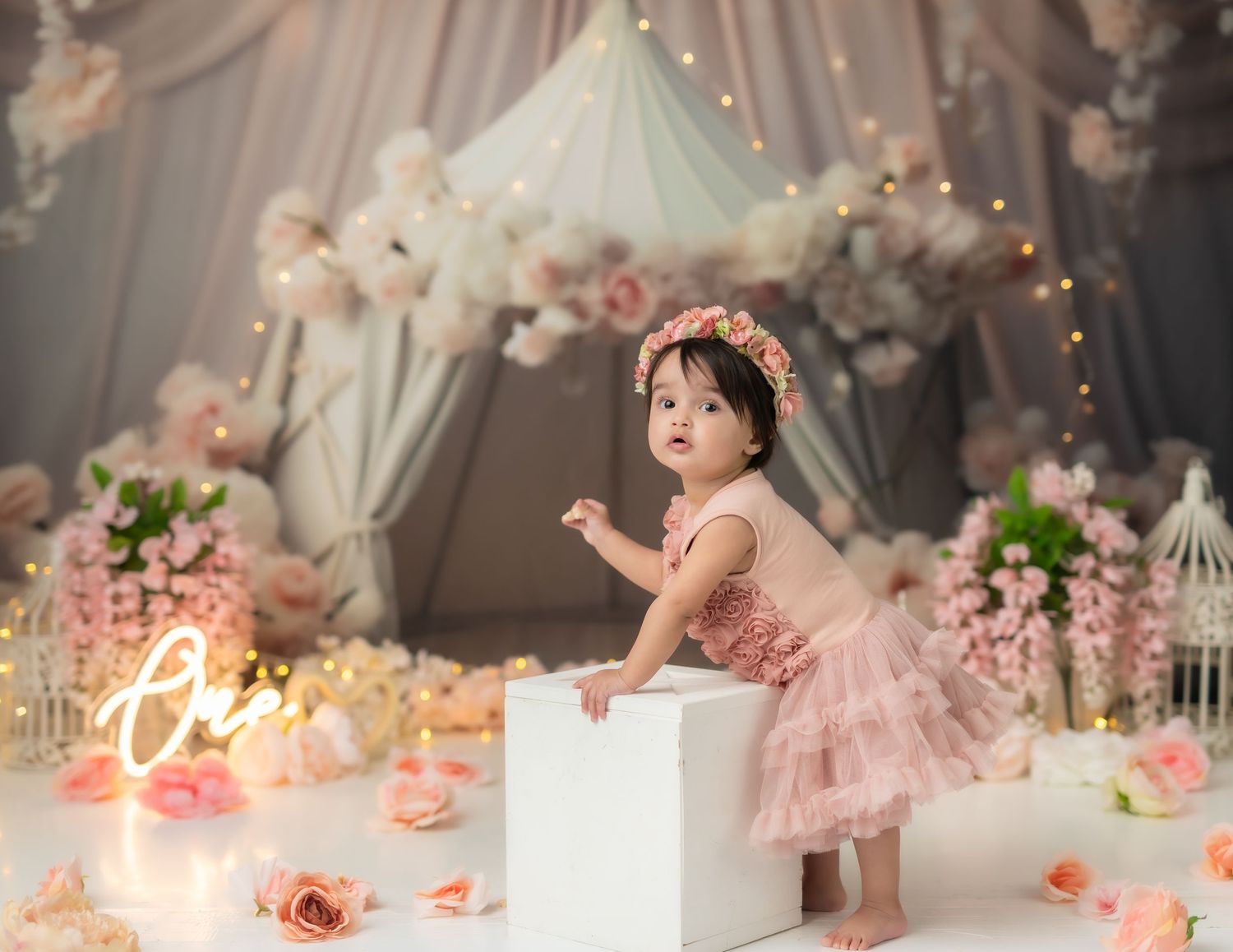 Elegant pink and white first birthday setup with tulle decorations and soft lighting.
