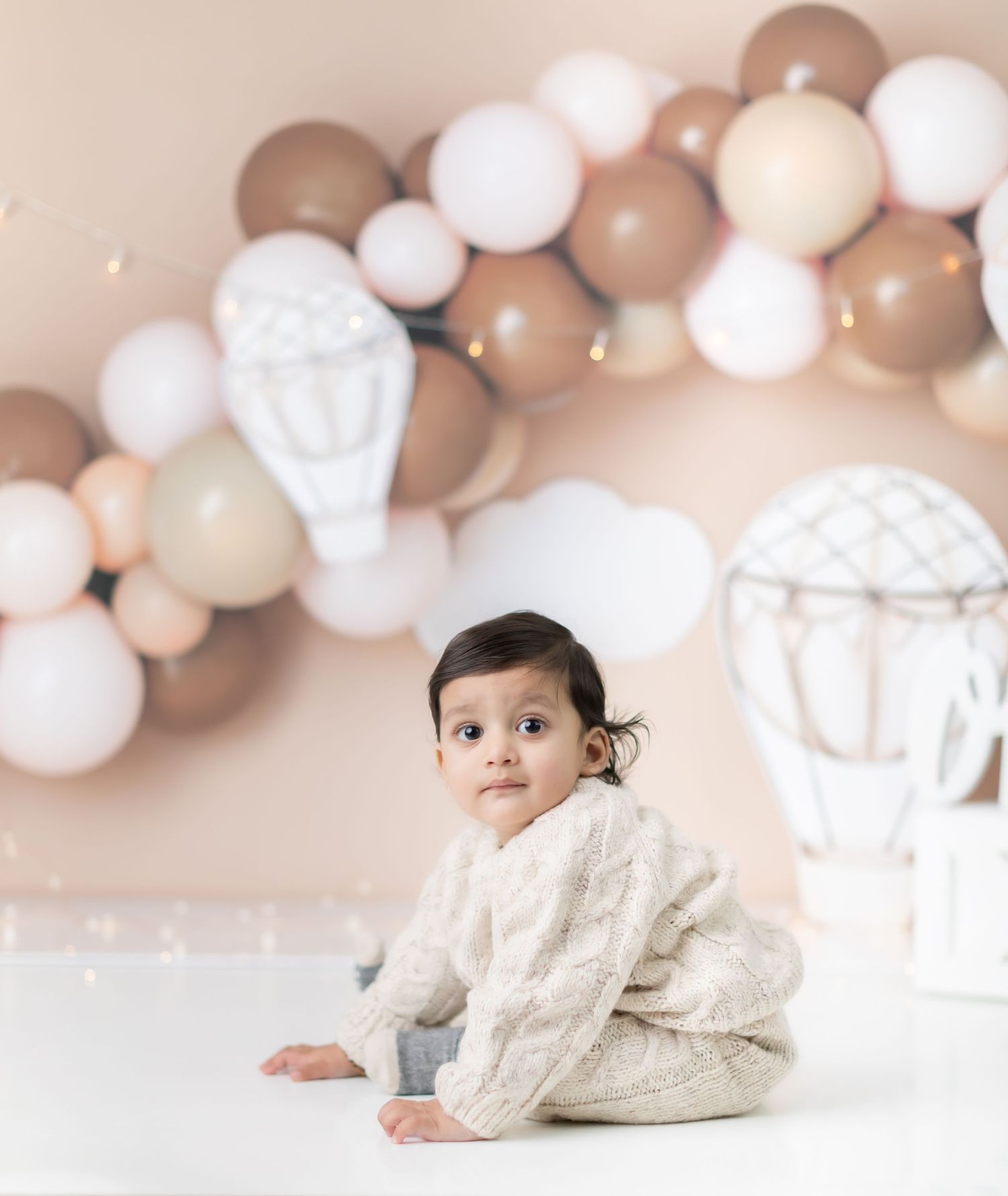 Neutral balloon arch with white hot air balloon decorations creates elegant backdrop.