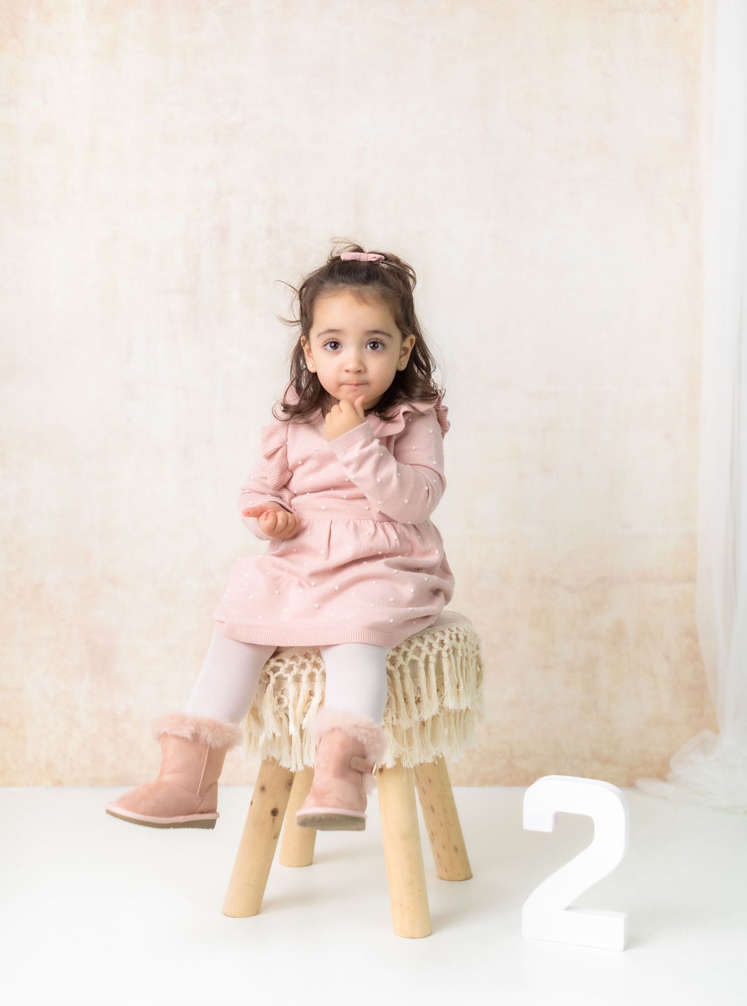 Wooden stool with macrame fringe detail against neutral backdrop with number 2.