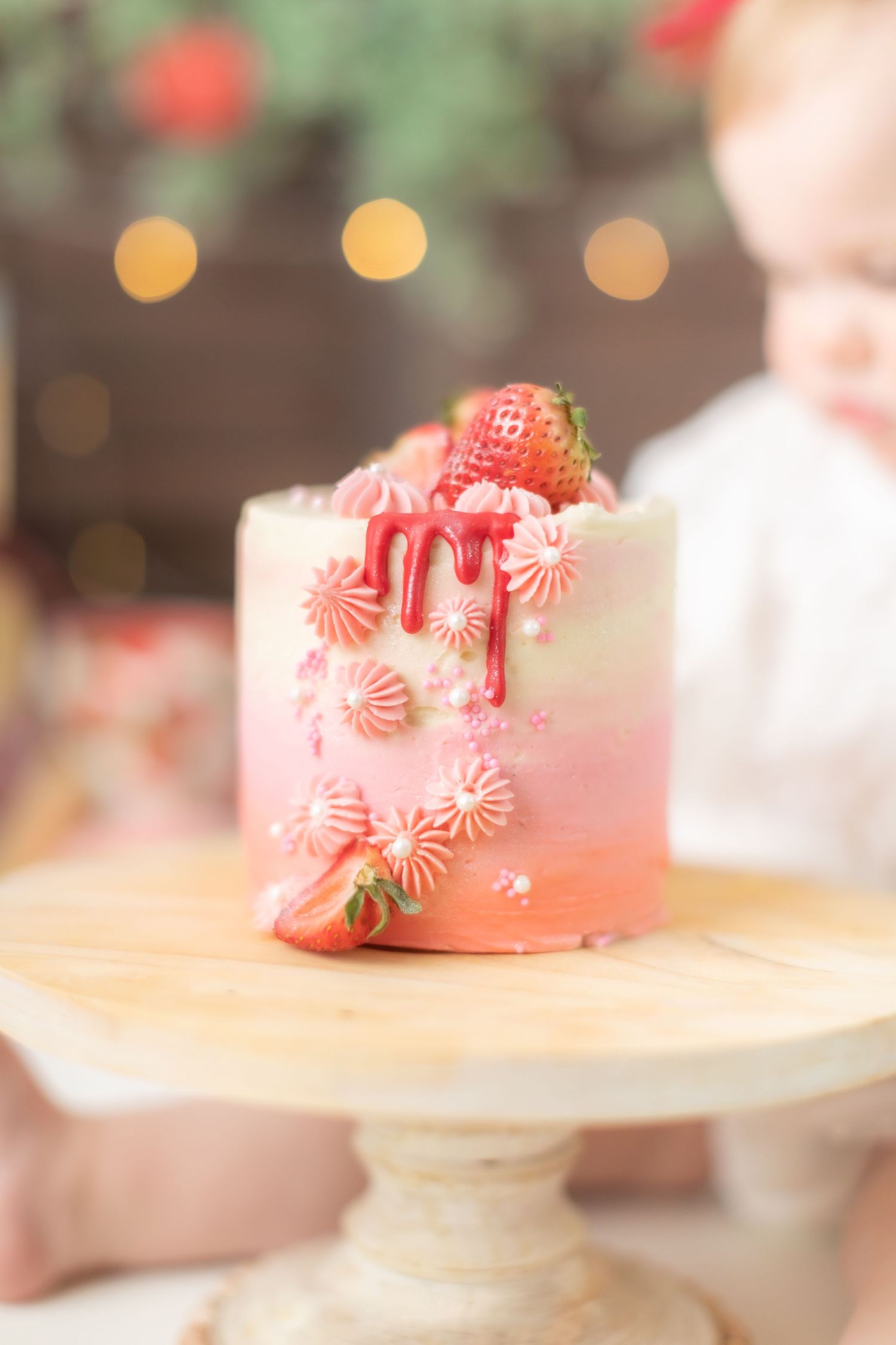 Pink strawberry cake on wooden cake stand with peppermint candy decorations.
