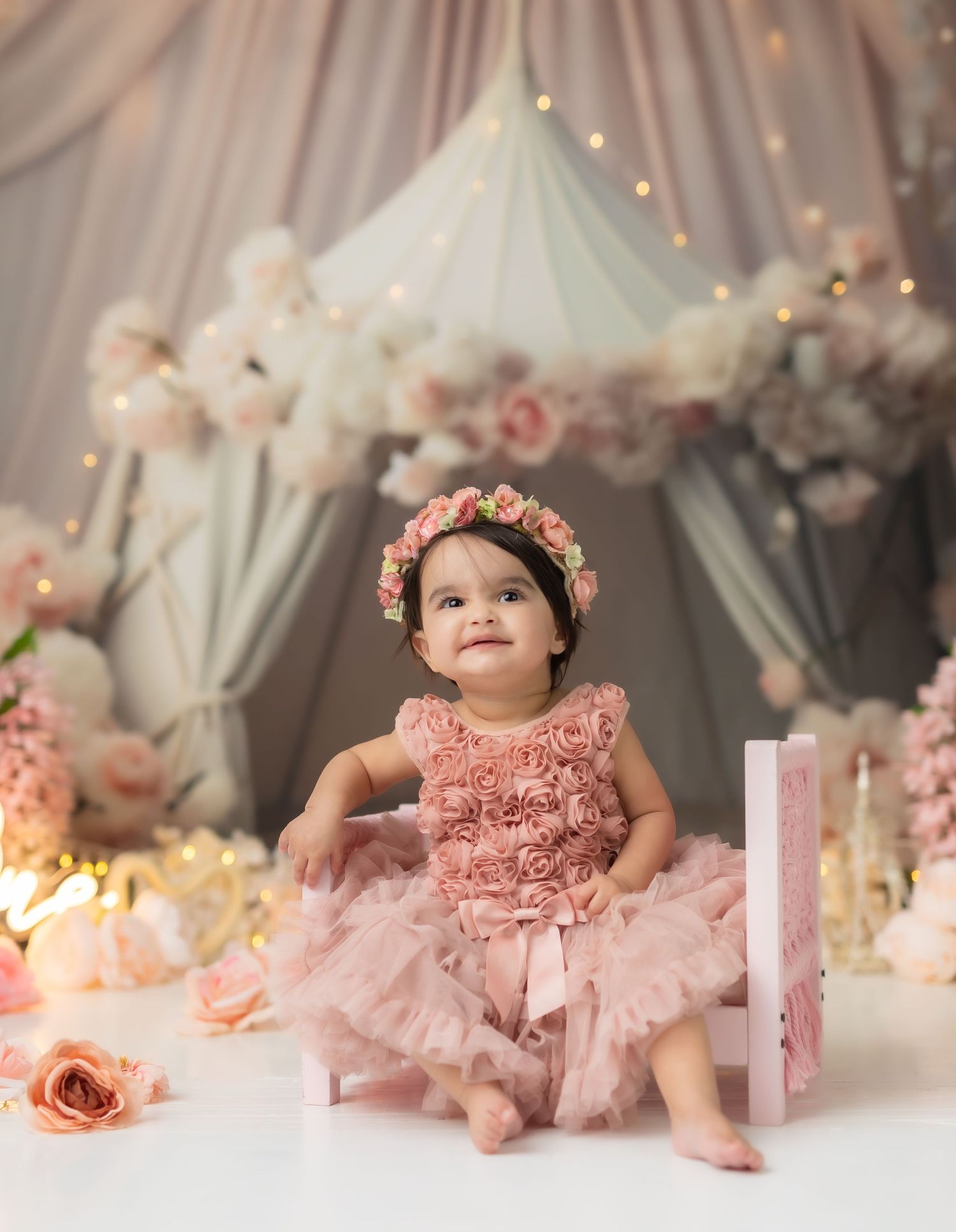 Baby in pink tulle dress and floral crown during first birthday cake smash photoshoot.