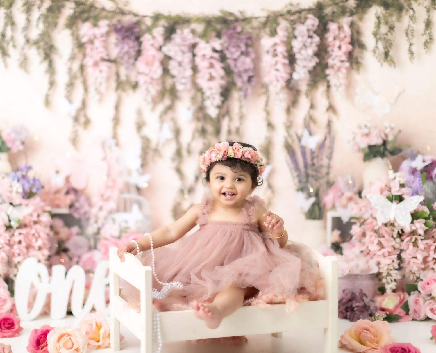 Dreamy cake smash photo setup with pink floral decorations and hanging wisteria.