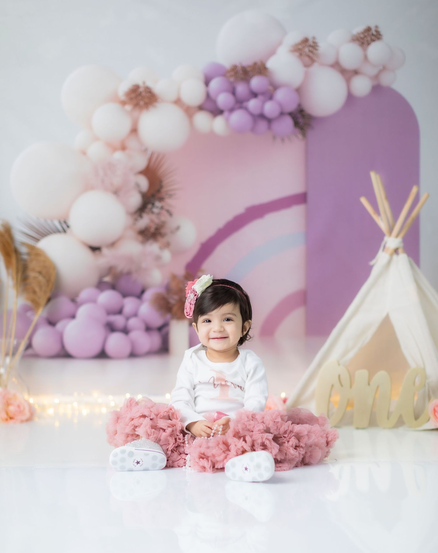 Purple and white balloon arch with teepee tent creates whimsical photography backdrop.