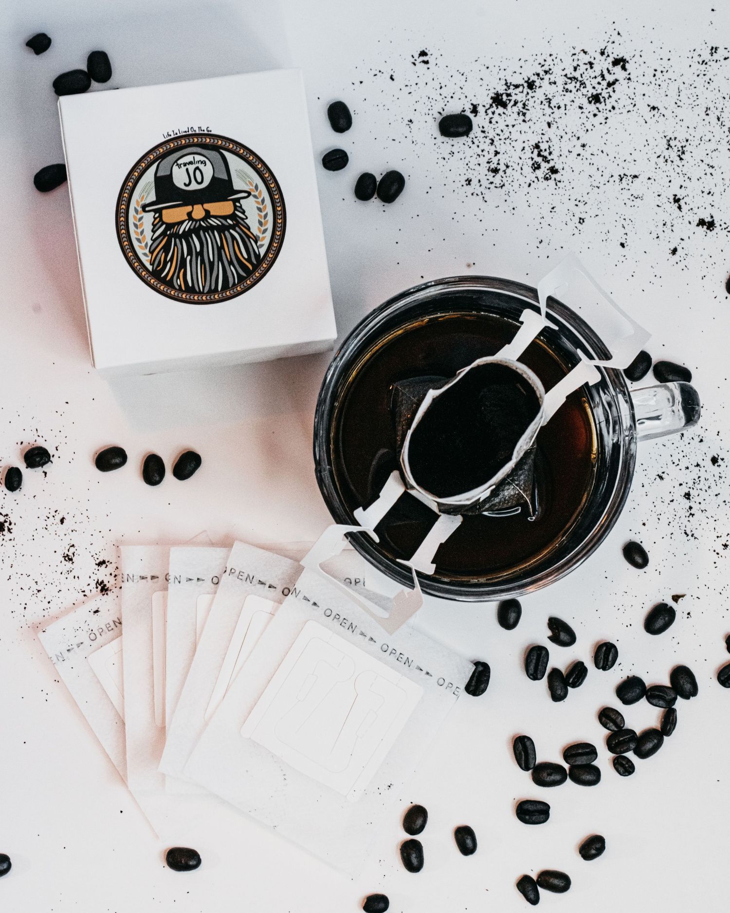 A box with logo, coffee beans, portable coffee filters, glass mug, and freshly poured coffee flat detail layout