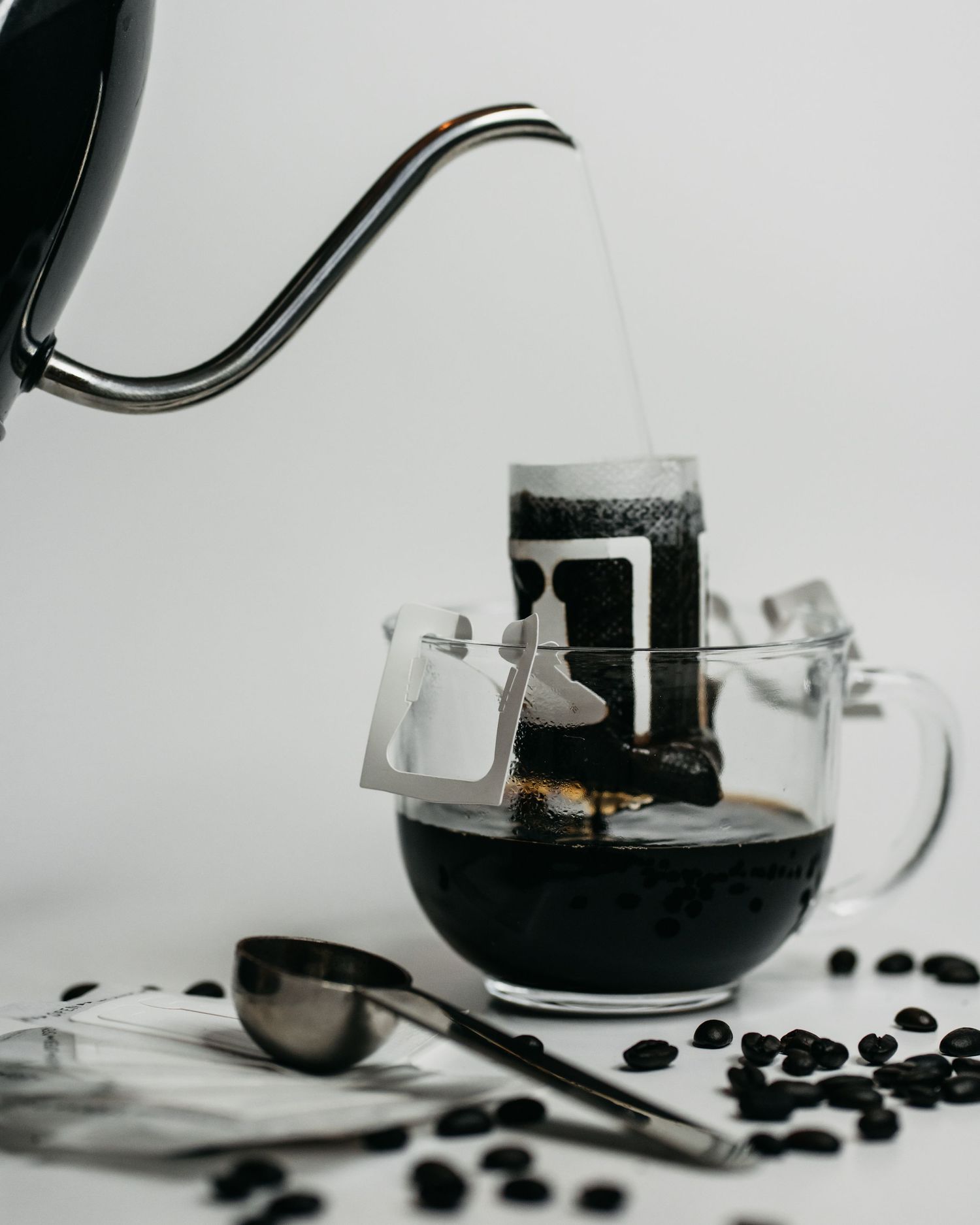 A glass mug holding a single light weight coffee filter with coffee and a kettle pours hot water over the coffee