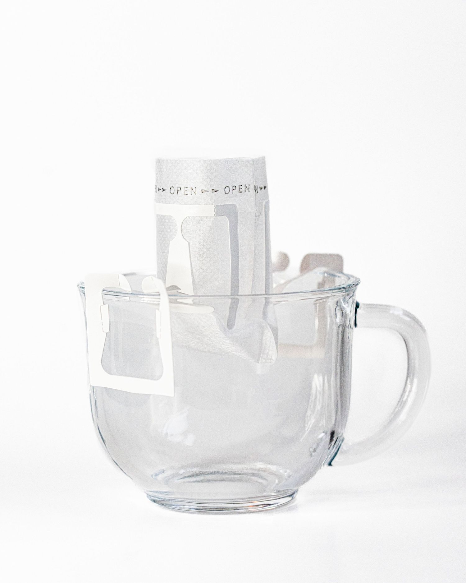 A glass mug in a white background holds a single lightweight pour over coffee filter