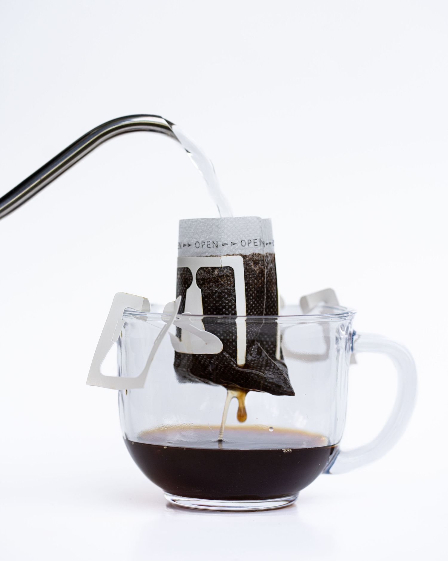 A kettle pours hot water over a portable coffee filter in a glass mug and coffee drips