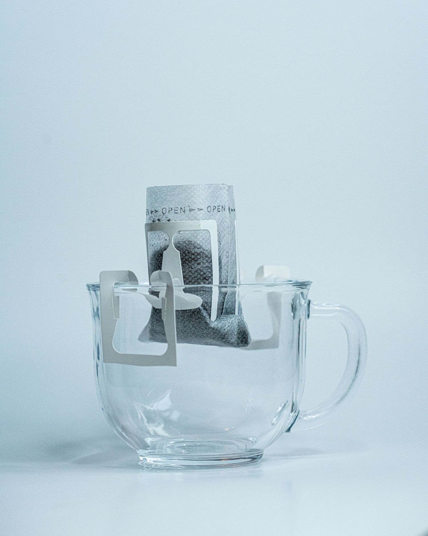 A glass mug in a white background holds a single lightweight pour over coffee filter with coffee grounds