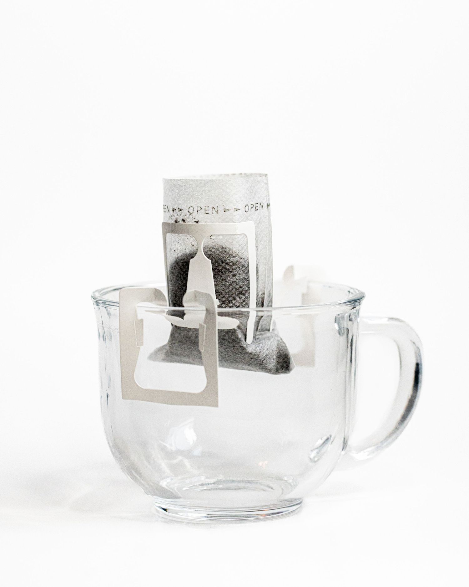 A glass mug in a white background holds a single lightweight pour over coffee filter with coffee grounds