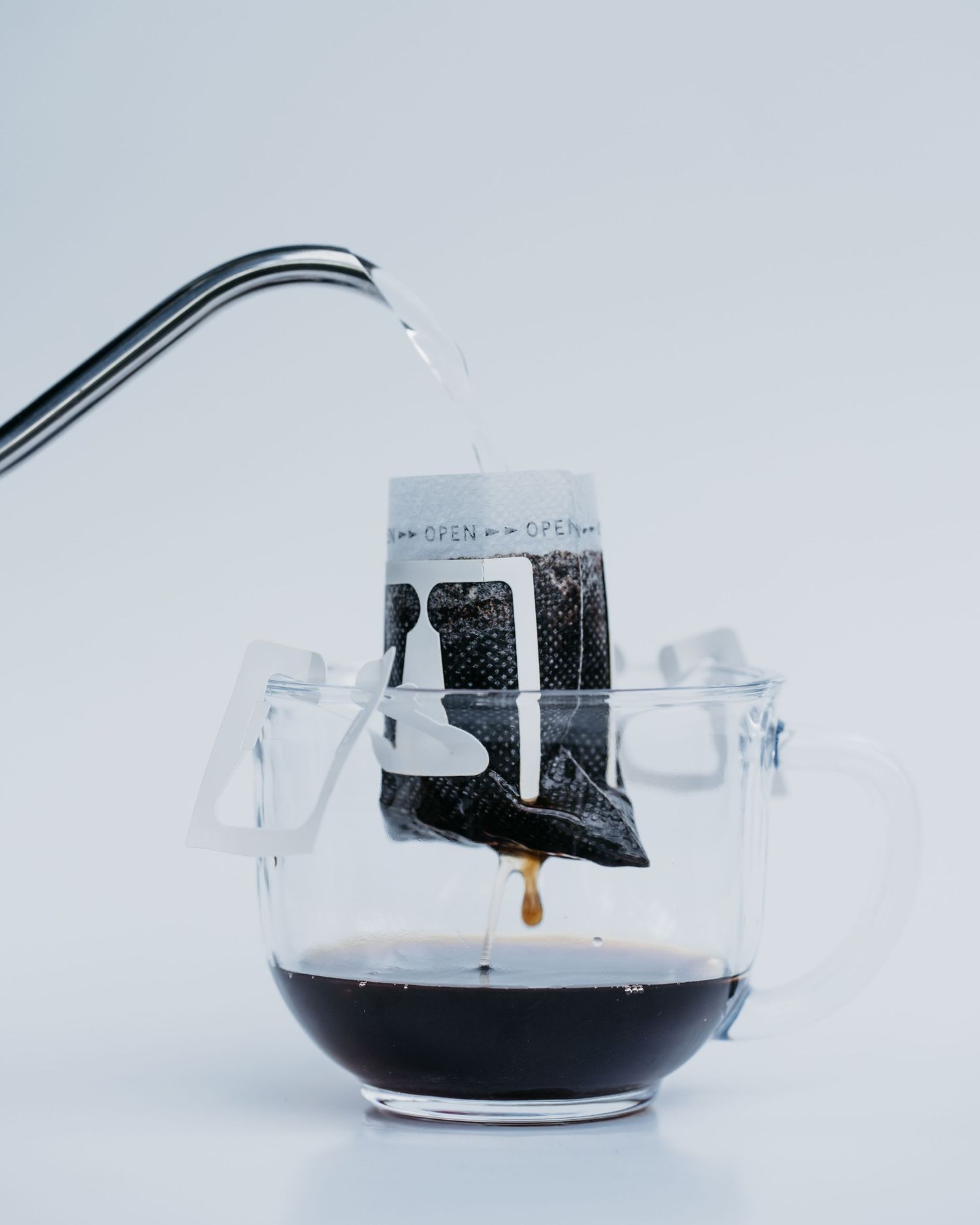 A glass mug with portable pour over coffee filter is dripping hot coffee into mug with kettle pouring water