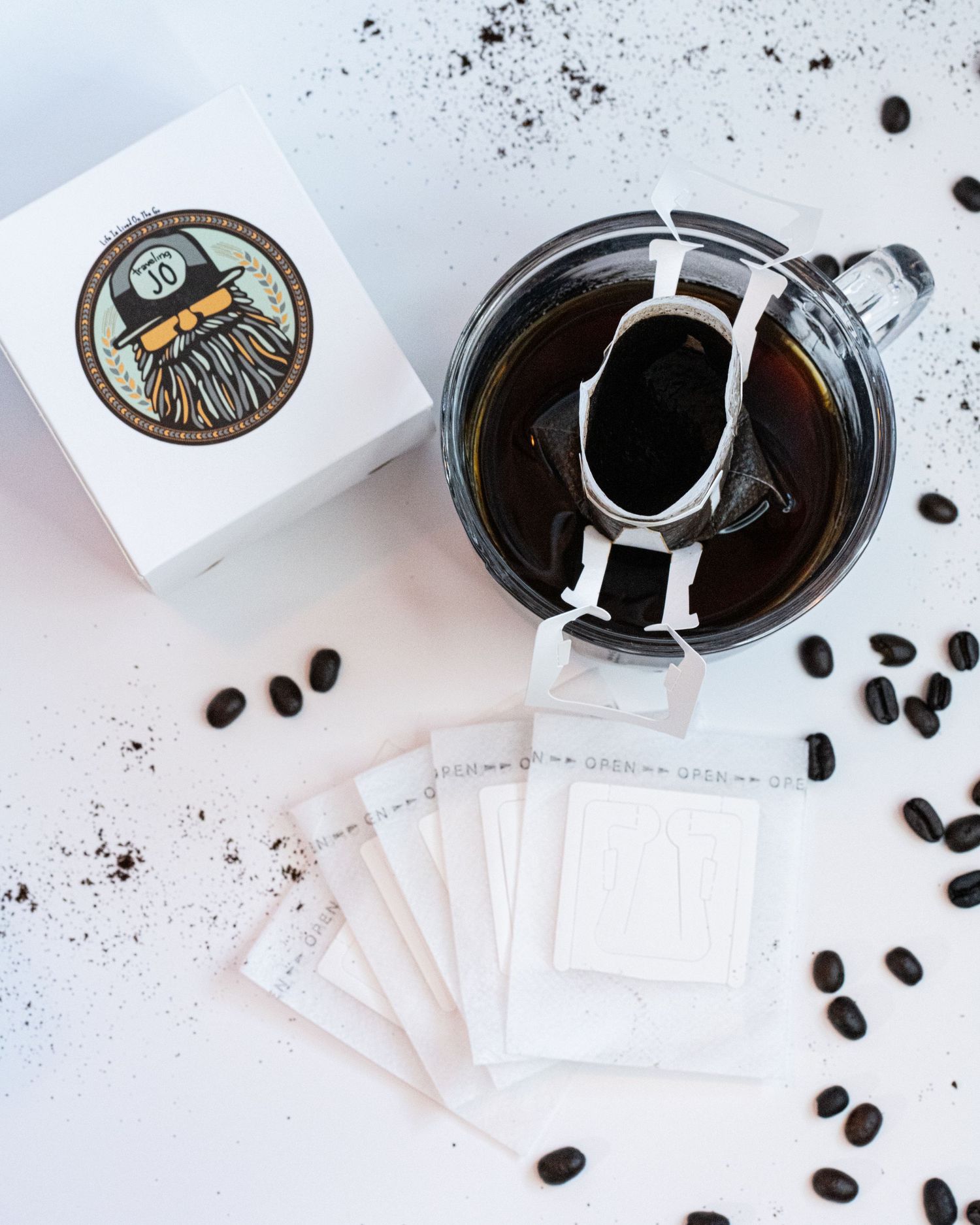 A box with logo, coffee beans, portable coffee filters, glass mug, and freshly poured coffee flat detail layout