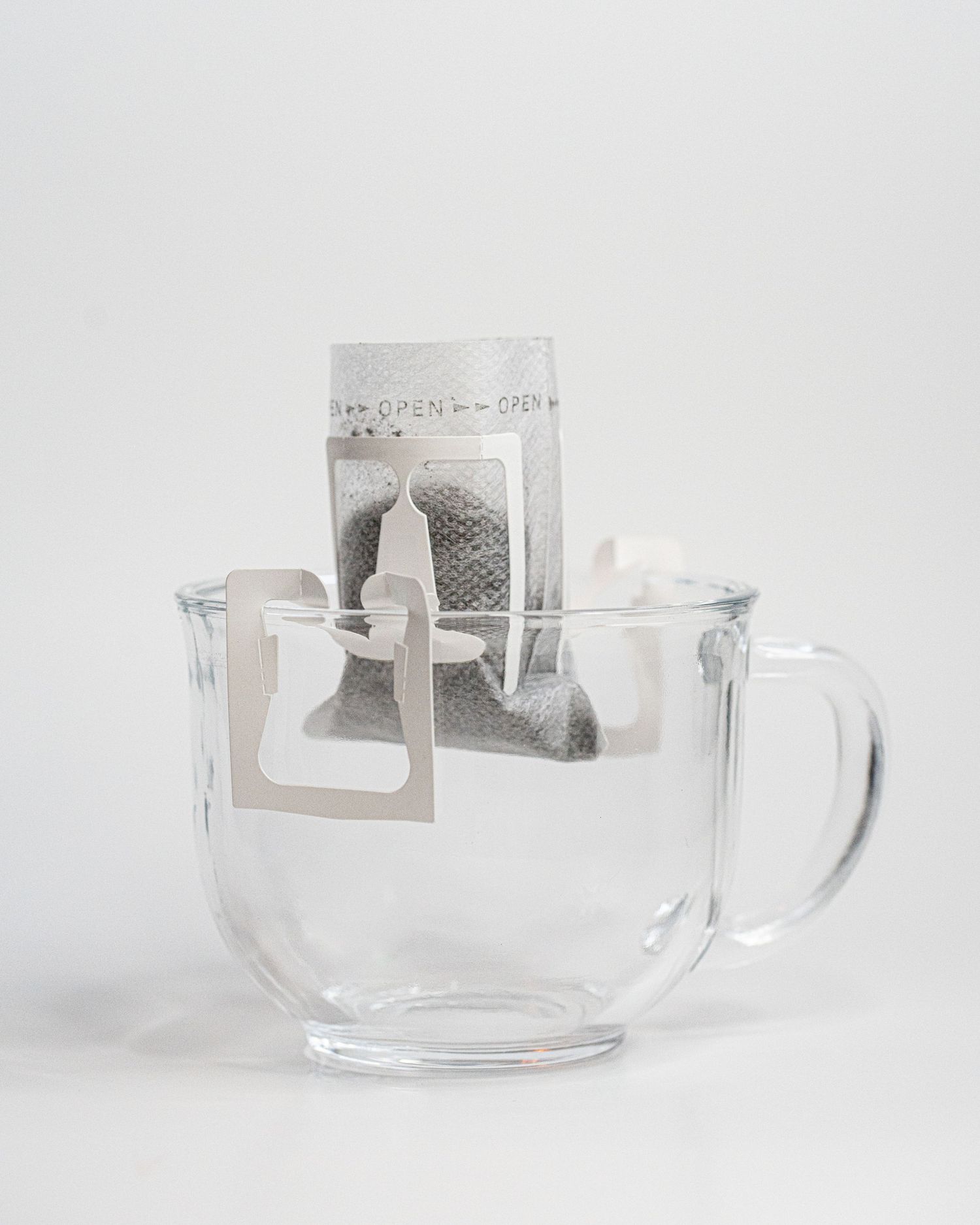 A glass mug in a white background holds a single lightweight pour over coffee filter with coffee grounds