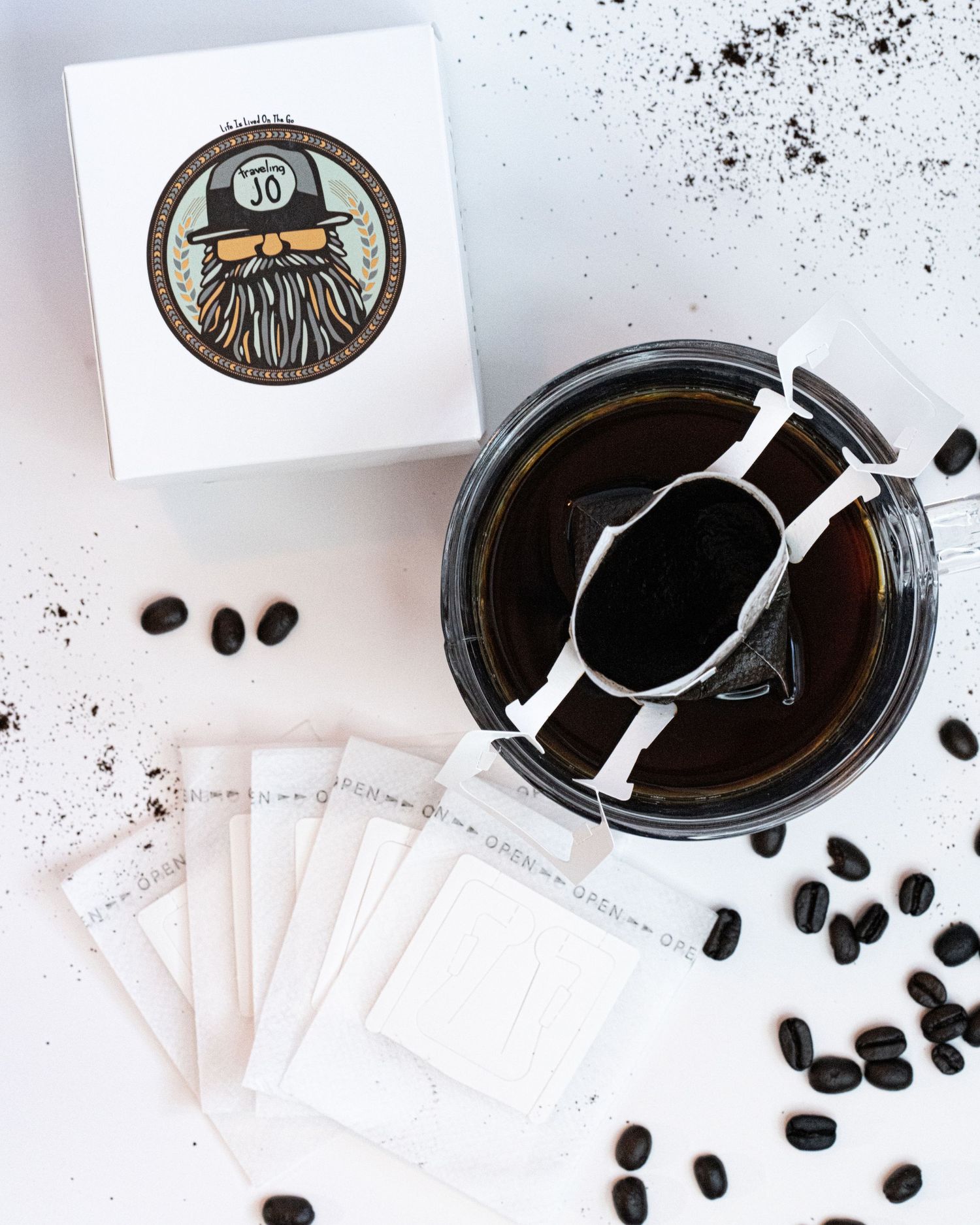 A box with logo, coffee beans, portable coffee filters, glass mug, and freshly poured coffee flat detail layout