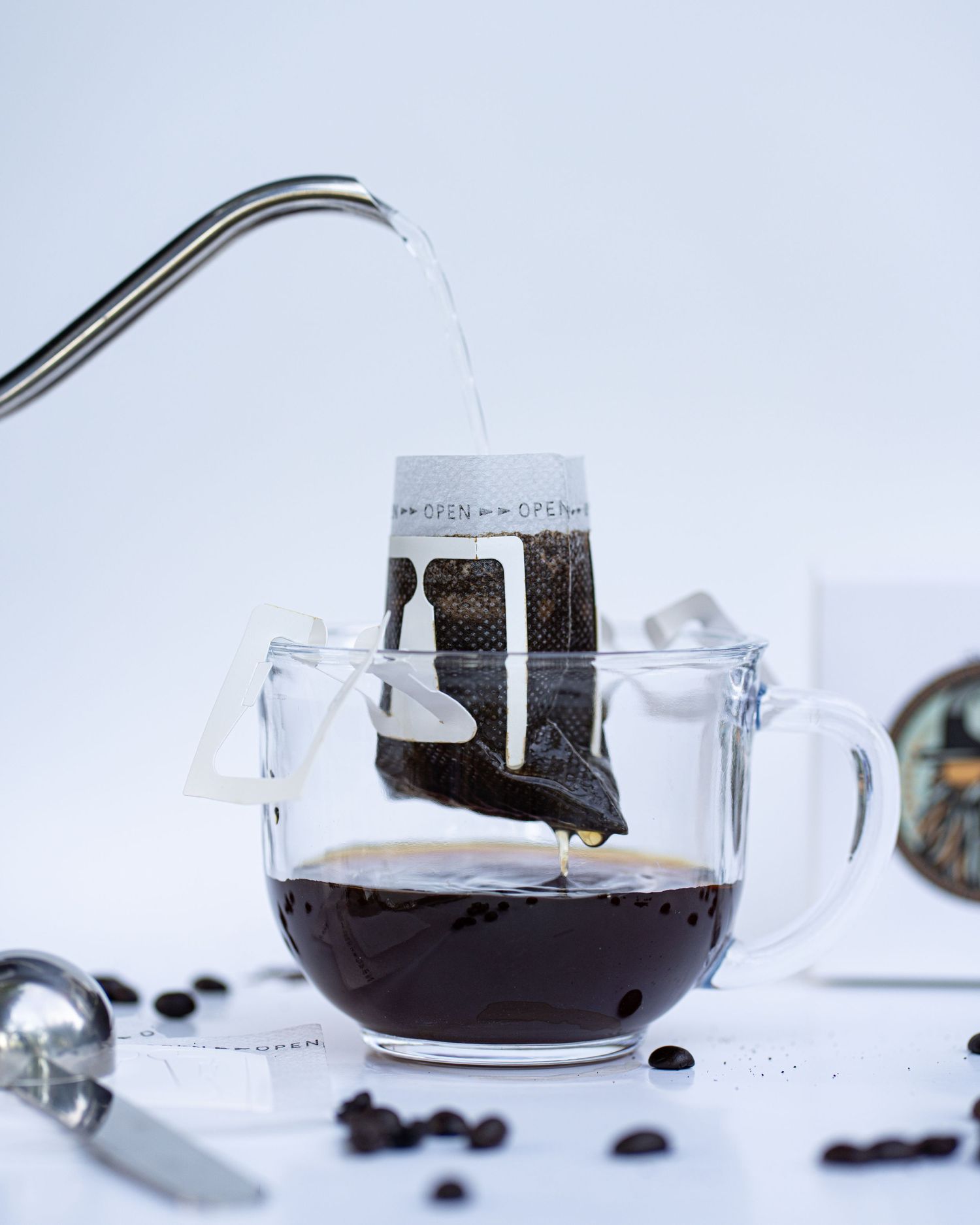 A kettle pours hot water over a portable coffee filter in a glass mug and coffee drips with coffee beans and scoop