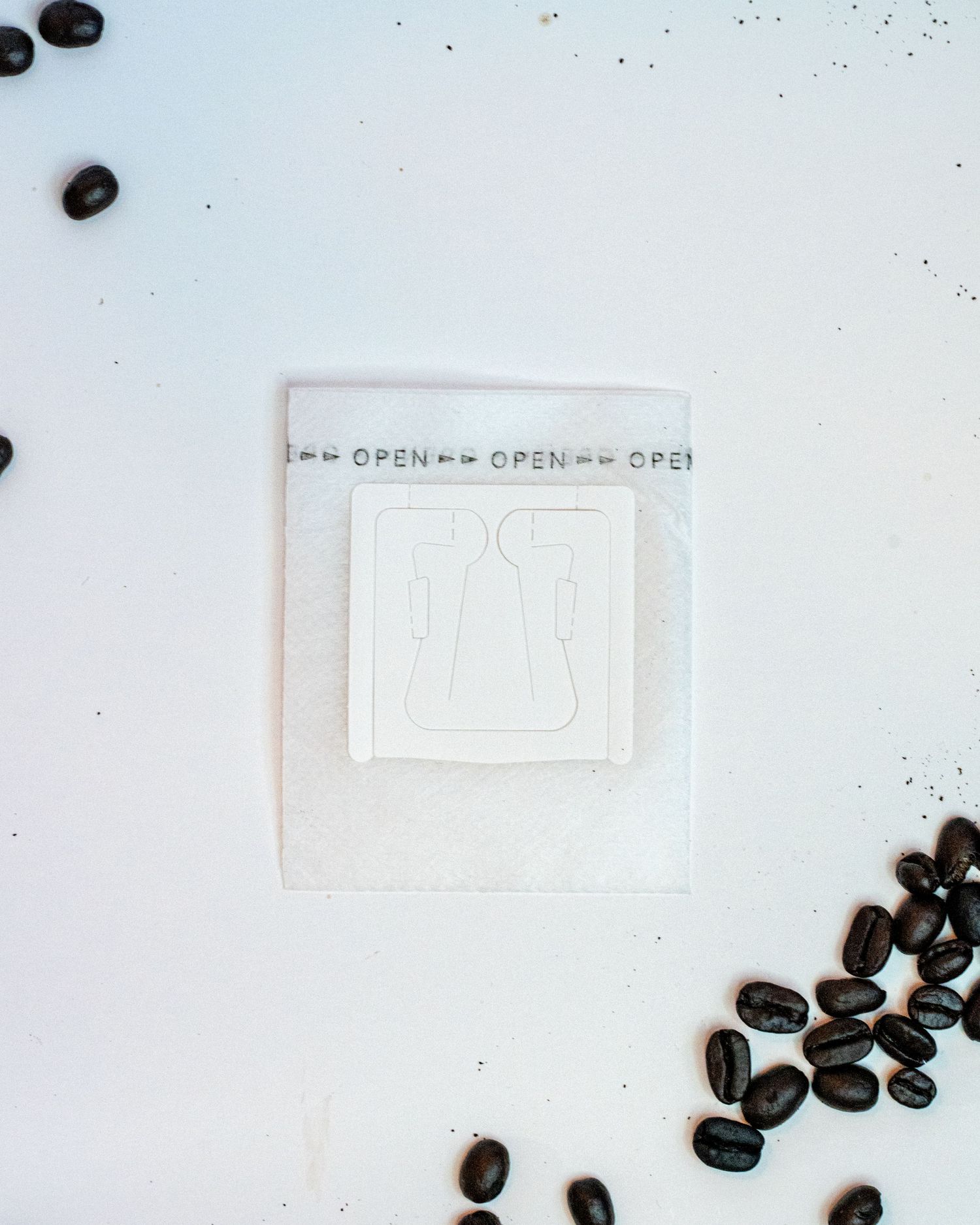 A flat detail layout of a portable pour over coffee filter on a white background with coffee beans on the edges