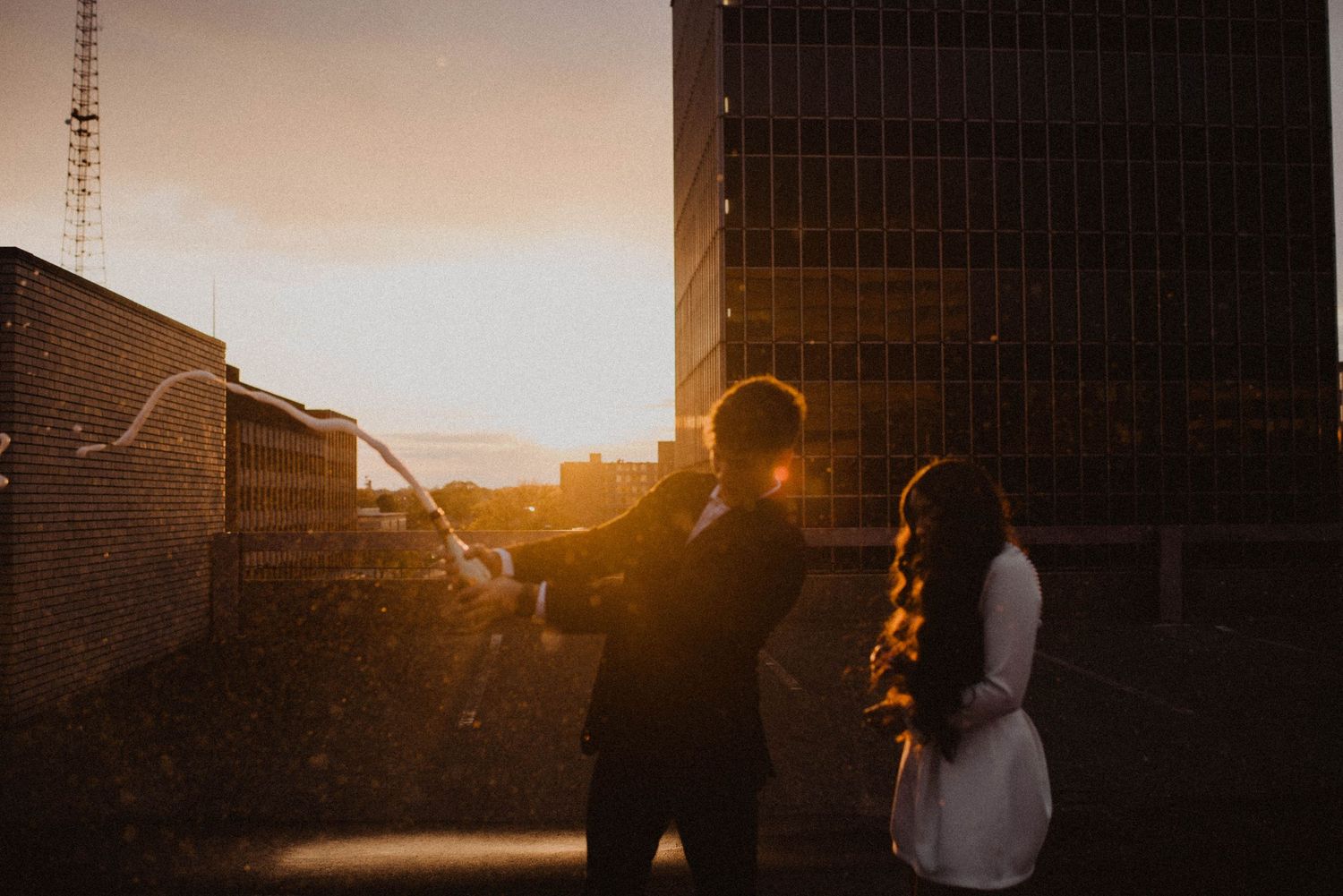 Silhouetted couple standing together against sunset and urban building backdrop.