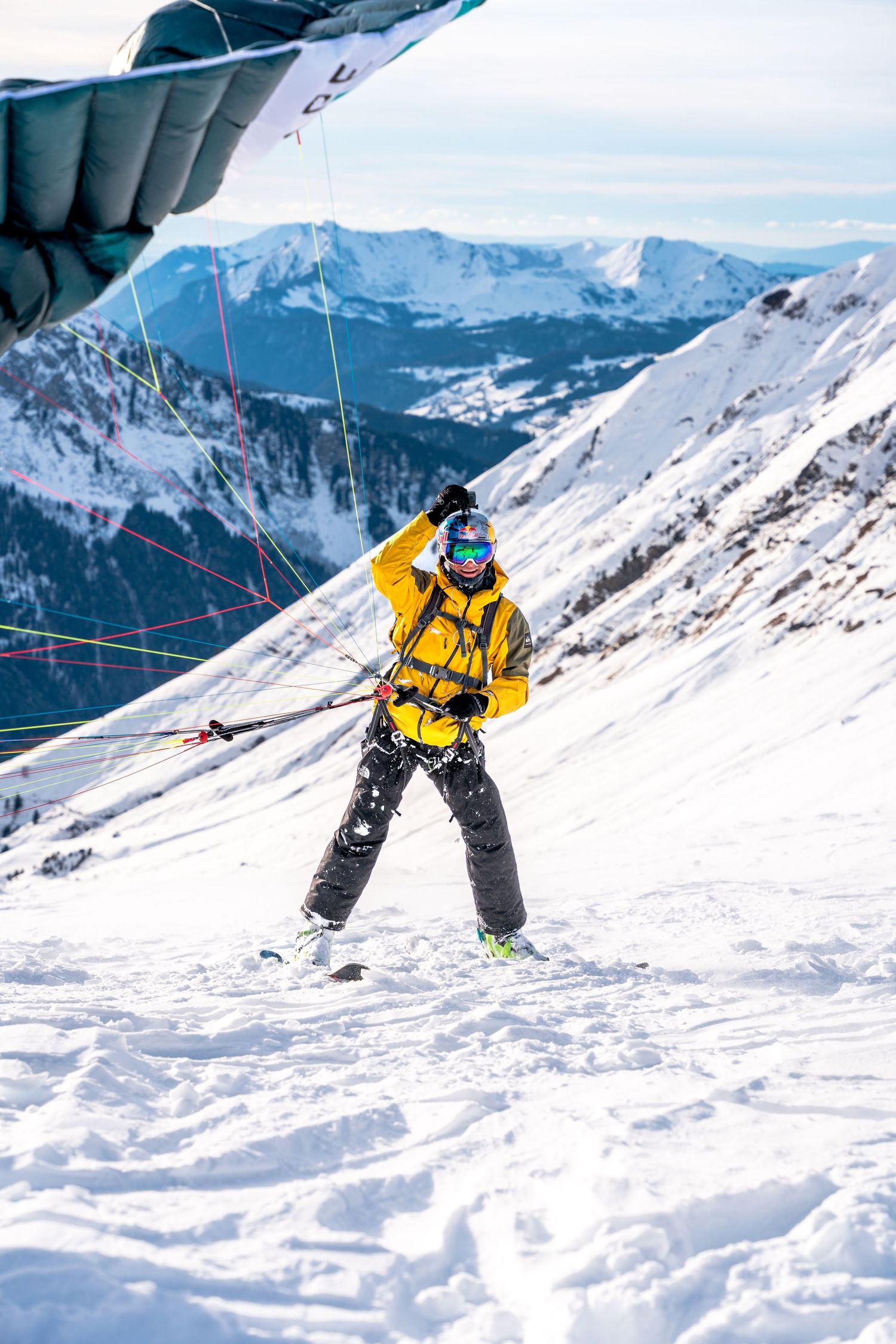 Skier in yellow jacket and safety gear descending snowy mountain slope.