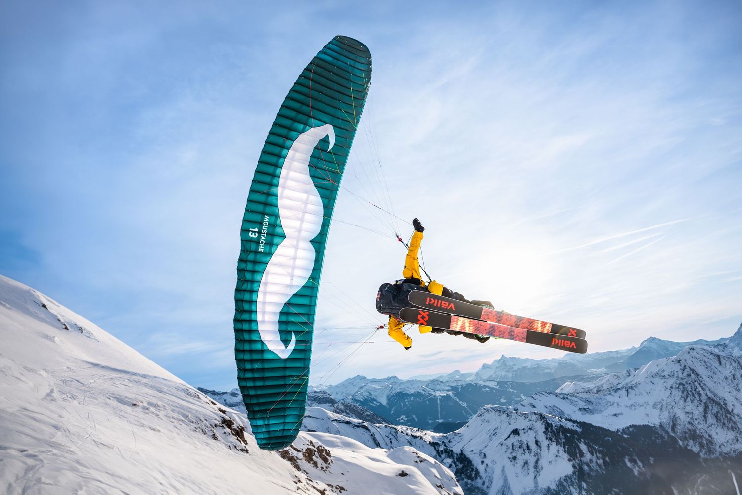 Snowkiter performing aerial jump with green parafoil against snowy mountain landscape.