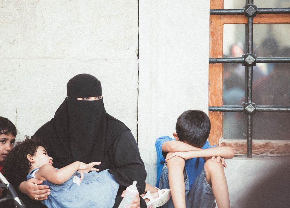Row of people sitting against white wall in indoor setting.