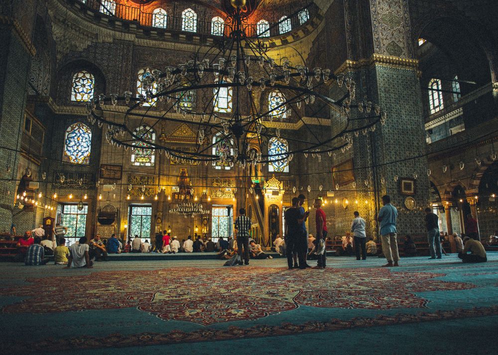 Interior of historic mosque with stained glass windows and hanging lanterns.