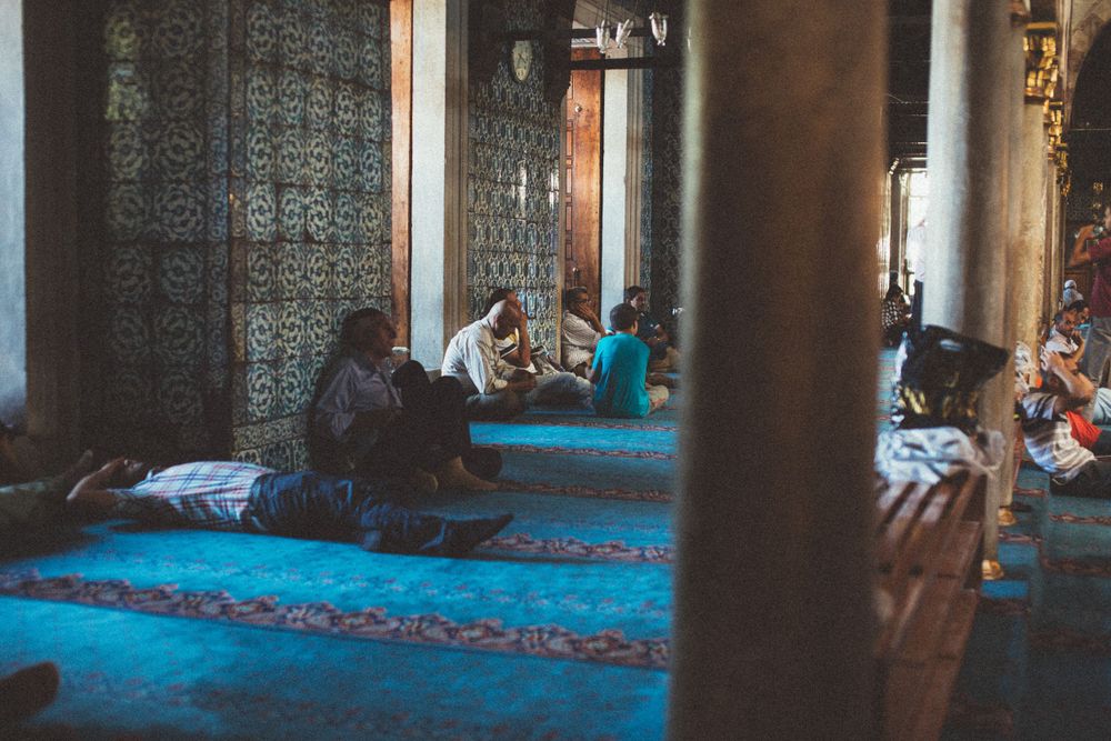 Interior of a grand mosque with ornate architecture and blue-tinted lighting creating a peaceful atmosphere.