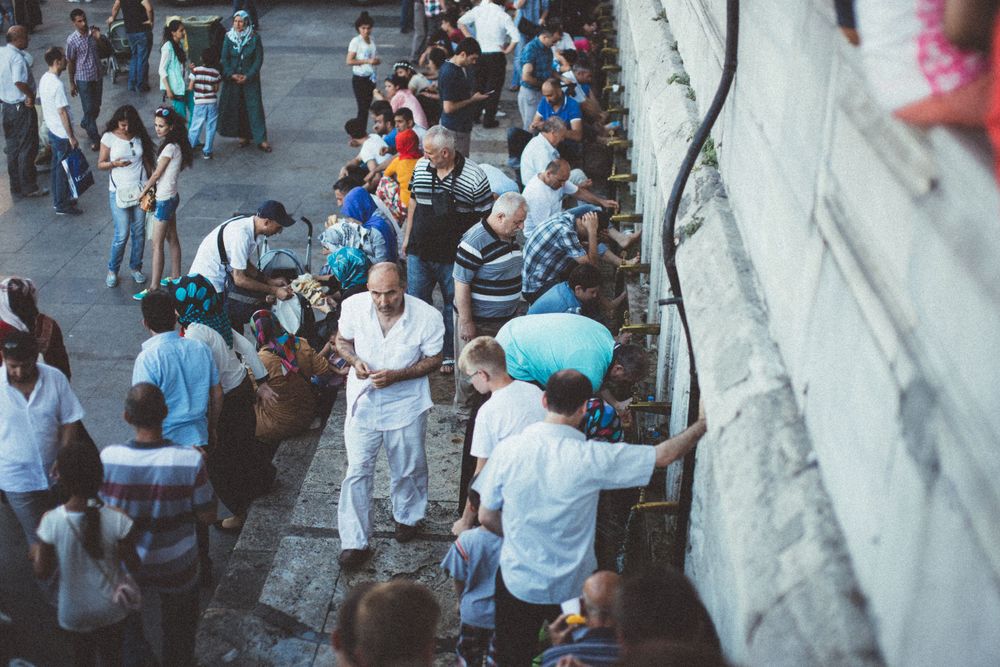 Crowd of people gathered along a stone wall in an urban setting.
