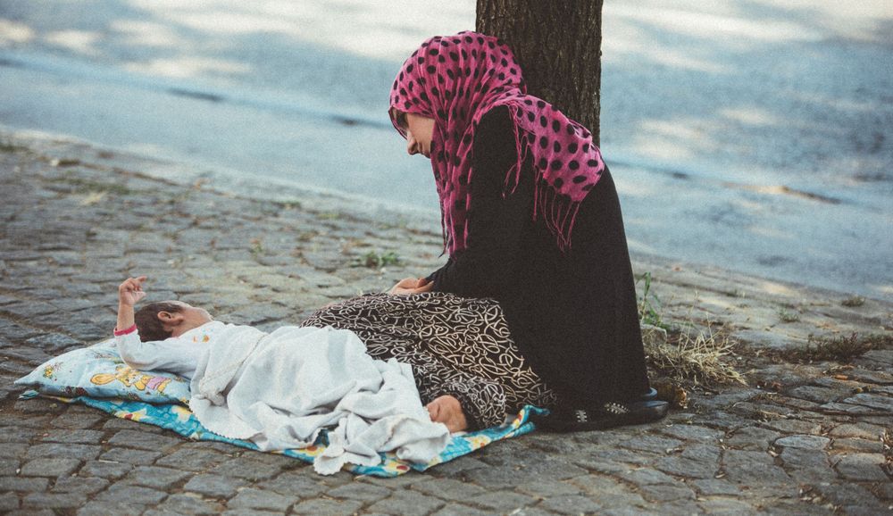 Person wearing a pink patterned dress sitting on cobblestone ground.