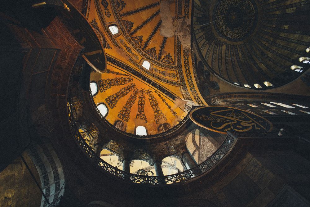 Ornate ceiling with golden geometric patterns and small windows in historic mosque.