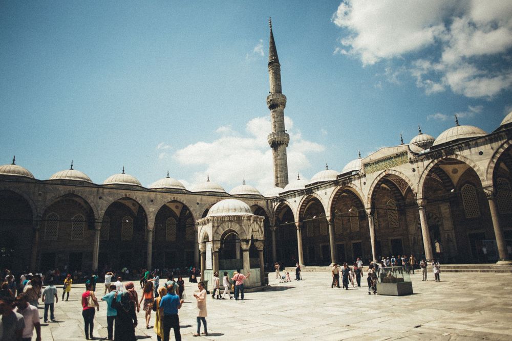 Panoramic view of Blue Mosque courtyard with arched colonnade under bright sky.
