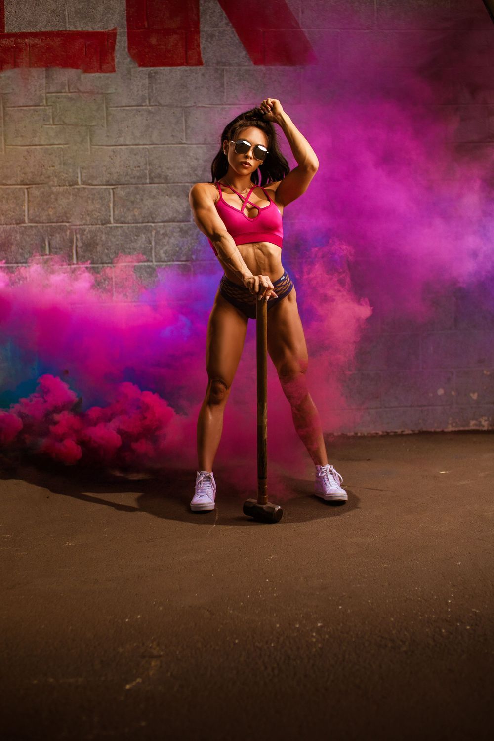Fitness model posing with golf club amid vibrant purple smoke against urban wall.