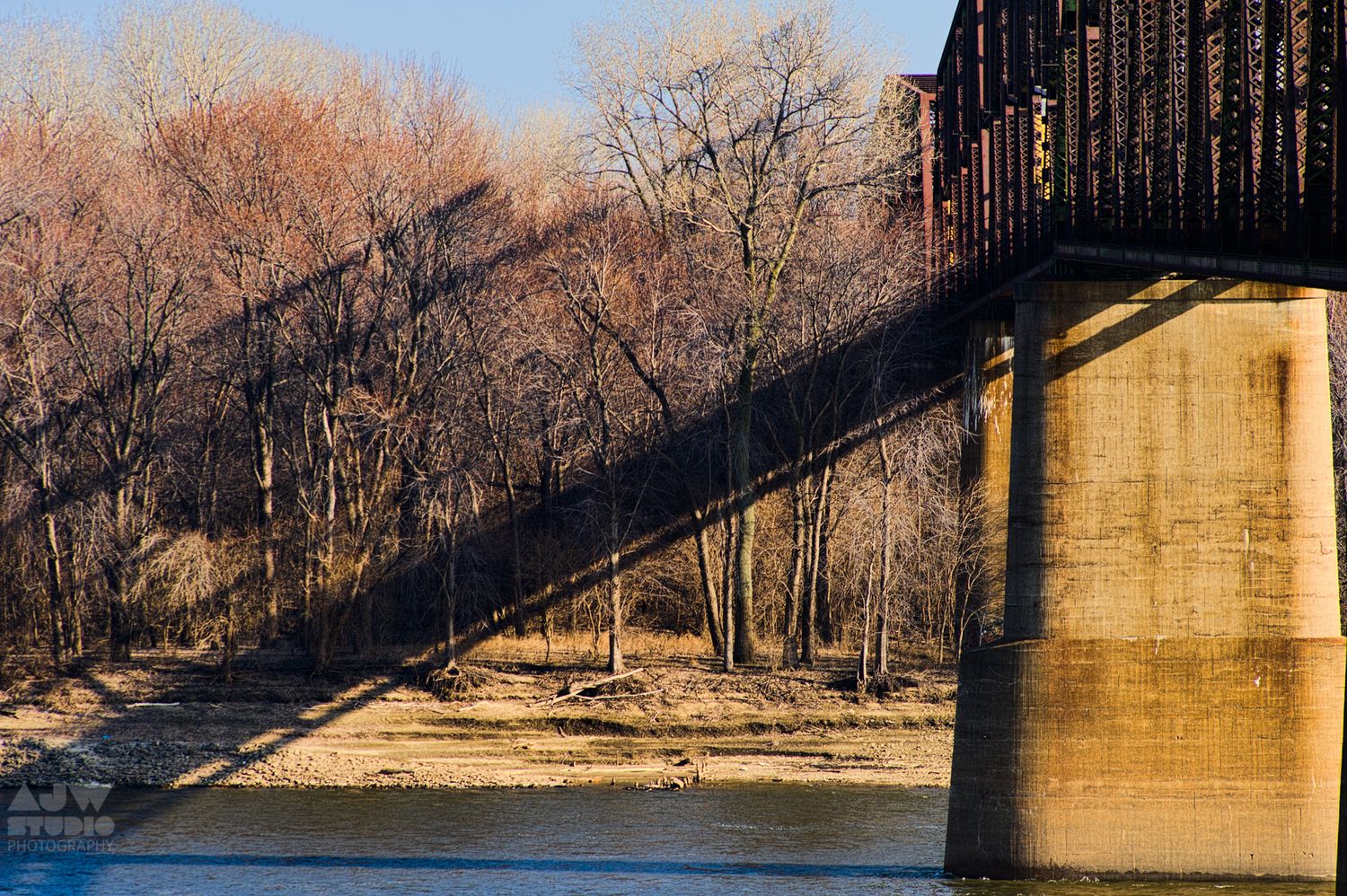 Railroad bridge crossing over river with bare winter trees in background.