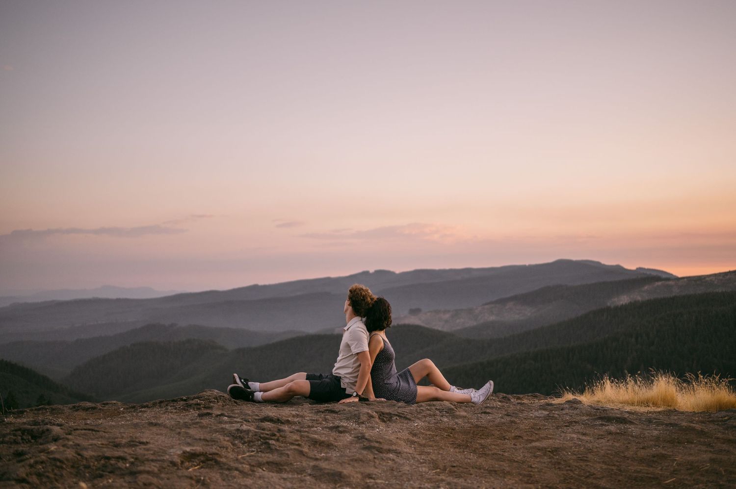 A couple sits on a mountain overlook during a dreamy sunset.