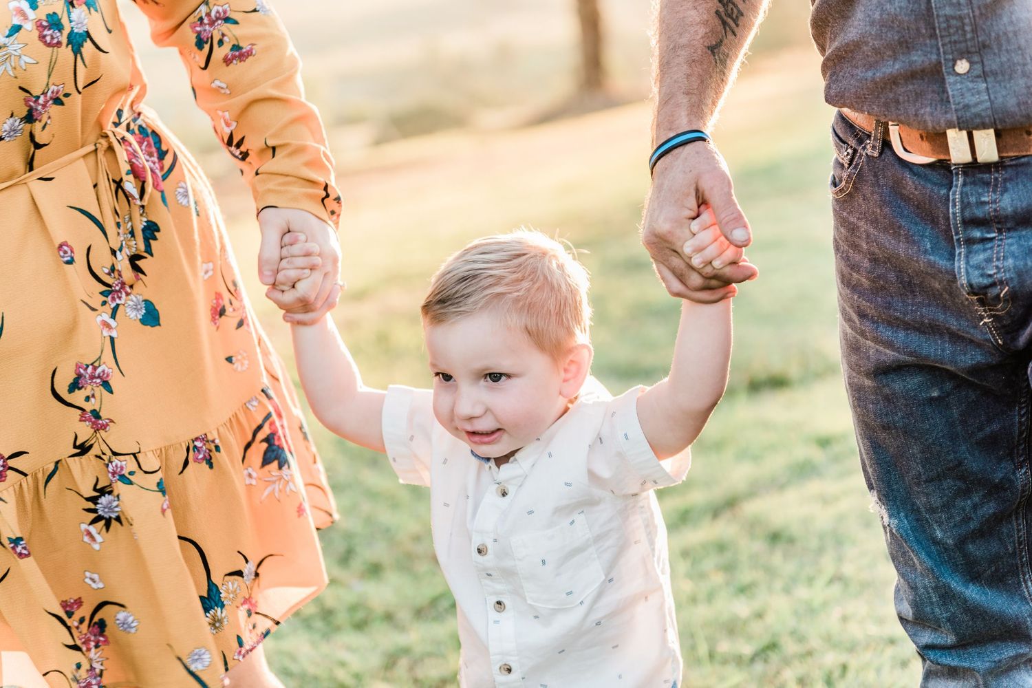A young child walking while holding hands with parents on a sunny day.