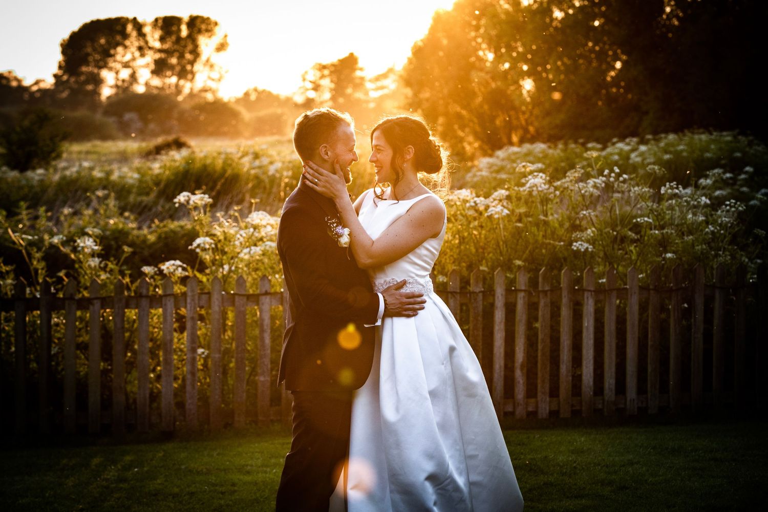 Golden sunset light illuminates couple in garden setting during wedding photoshoot.