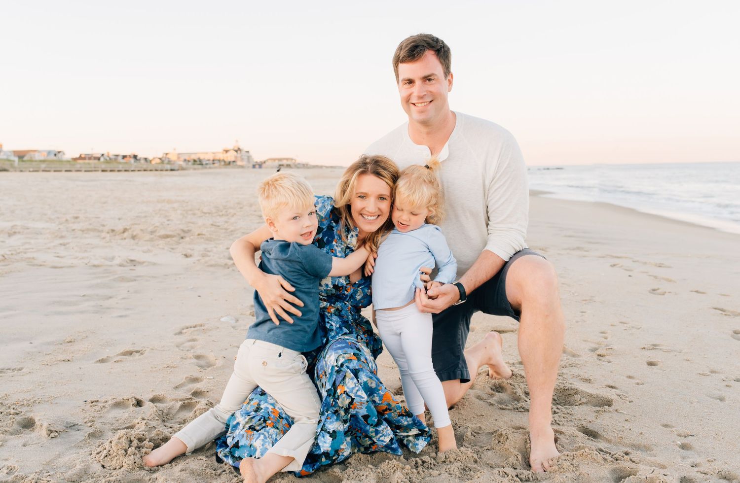 A fun family cuddles together in a big bear hug while playing on the beach.