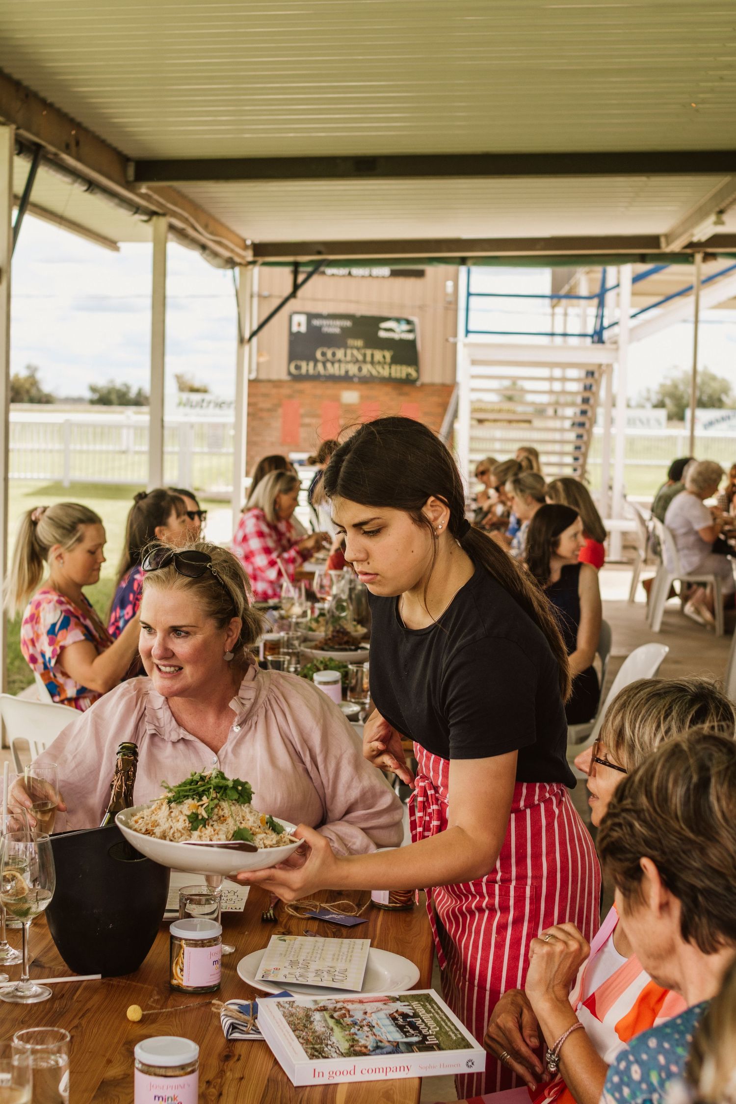 Rural women sitting around tables outdoors at the Coonamble Jockey Club attending the In Good Company Long Lunch event