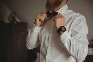 Person adjusting bow tie while wearing crisp white dress shirt and watch.