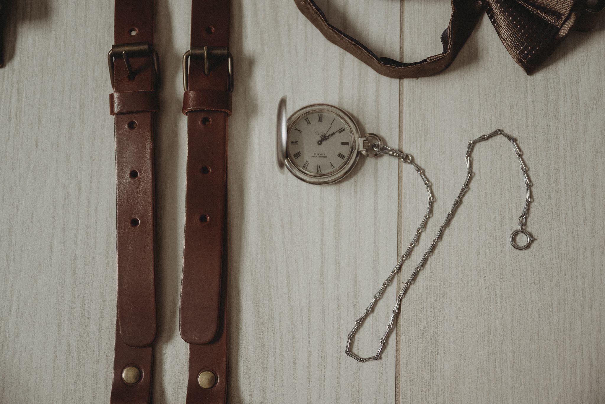 Vintage pocket watch with chain laid out with leather straps on a white wooden surface.